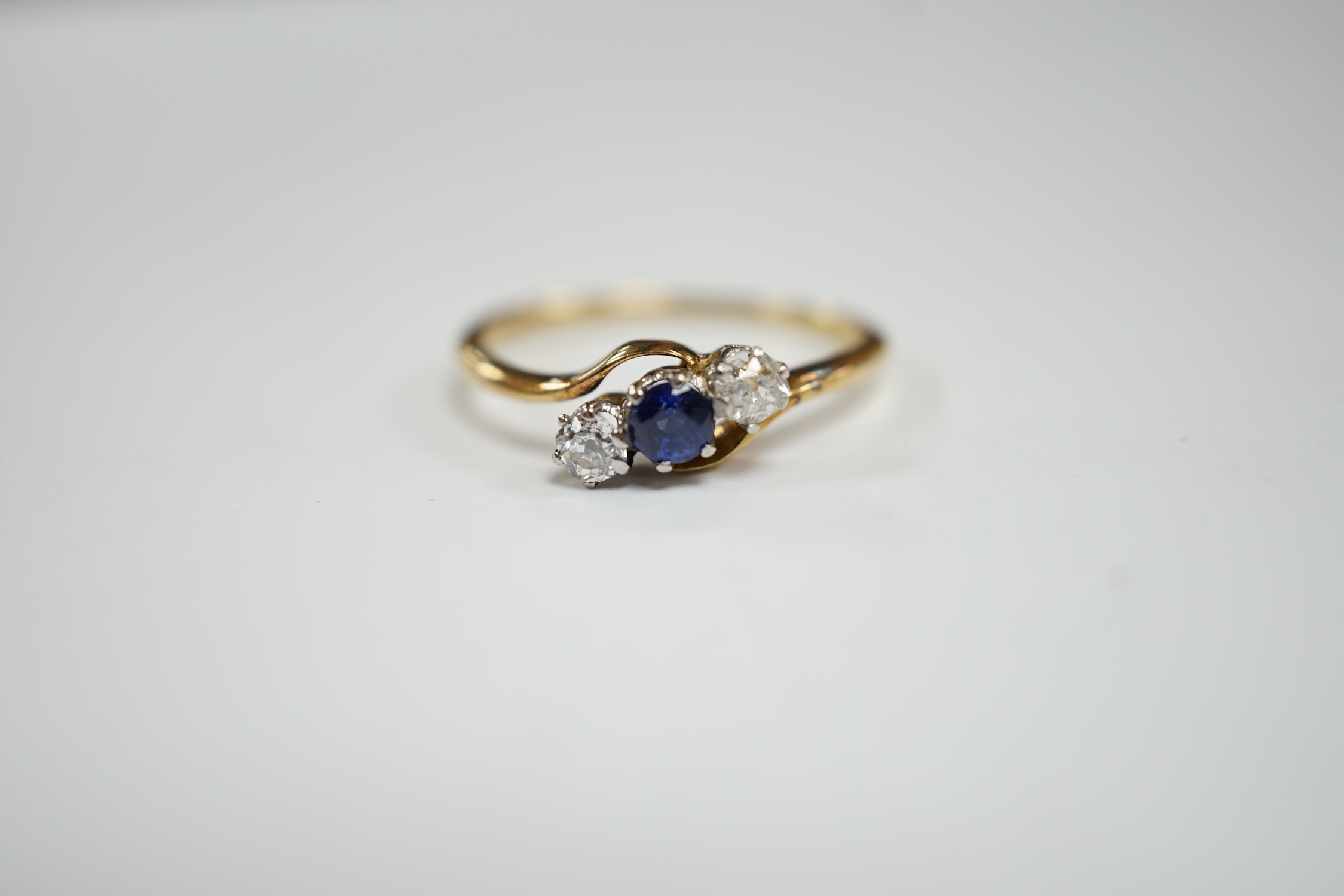 An 18ct, single stone sapphire and two stone diamond set crossover ring, size O, gross weight 2.2 grams.